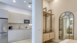 Une chambre moderne avec un grand lit, un dressing et un coin cuisine doté de meubles blancs et d’un four à micro-ondes.