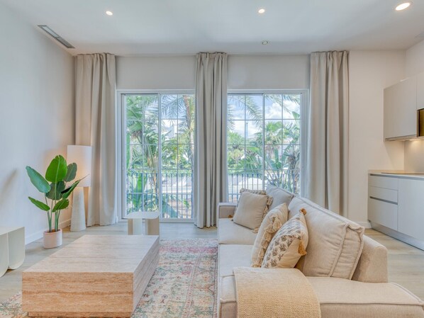 Ein modernes Wohnzimmer mit Sofa, Couchtisch und Blick auf einen Balkon mit Pflanzen.