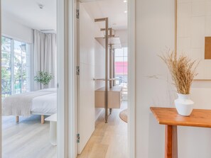 Ein modernes Hotelzimmer mit Bett, Nachttisch aus Holz, einer Vase mit Trockenpflanzen und Blick ins Freie.