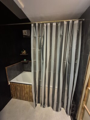 Et moderne badeværelse med badekar, bruseforhæng og en lille hylde med toiletartikler.