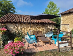 Eine Terrasse mit Steinmauern, einem Ziegeldach und Gartenmöbeln.