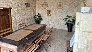 Une pièce rustique avec un mur en pierre, une table en bois surmontée d’un tapis en fibres naturelles, deux chaises et des plantes en pot.