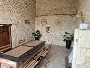 A rustic room with a stone wall, a wooden table with a woven mat, two chairs, and potted plants. - GITE IN THE HEART OF THE PERIGORD BLANC FOR UP TO 6 PEOPLE (Neuvic)