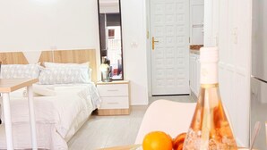 Een hotelkamer met een bed, nachtkastje, een eettafel met eten en drinken, en een deur.