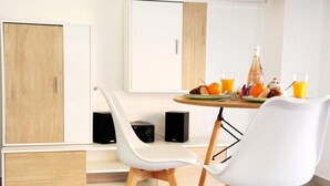 Een moderne eetruimte met een tafel gedekt voor twee personen, twee witte stoelen, een speaker en een kast.