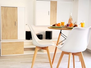 A modern dining area with a table set for two, two white chairs, a speaker, and a cabinet. - Modern studio 50m from the beach with air conditioning (Los Cristianos)