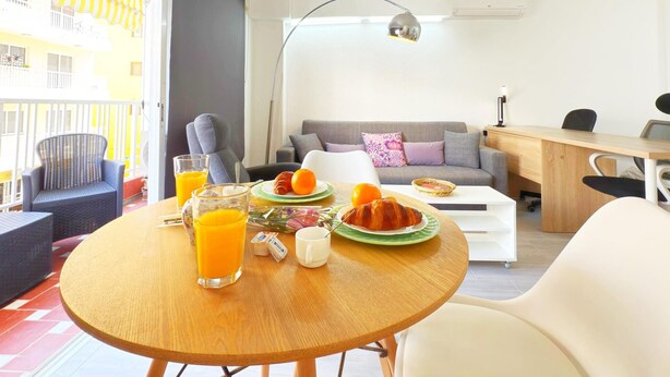 Een moderne woonkamer met een eettafel, een bank, een bureau en een balkon met uitzicht op een gebouw.