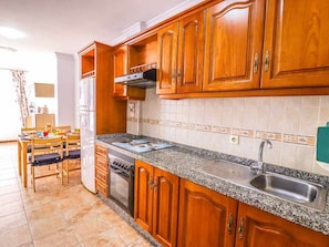 A kitchen with wooden cabinets, a granite countertop, a stainless steel sink, and a dining area with a table and chairs. - Apartment in Playa San Juan, near beach, wifi, parking (Playa San Juan)