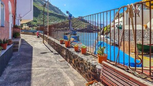 Une propriété située sur la côte, dotée d’un mur en pierre, de plantes en pot et offrant une vue sur la mer et les montagnes.