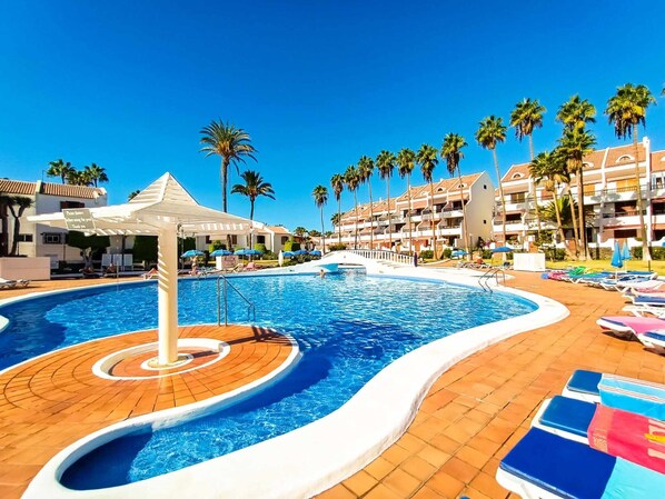 Ein Poolbereich eines Resorts mit einem runden Pool, Liegestühlen und Palmen.