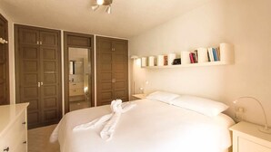 Una habitación de hotel con cama, mesitas de noche, un armario y una estantería con libros.