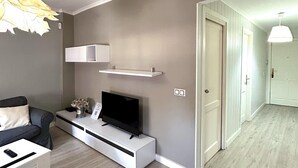 A modern living room with a flat-screen TV on a white console, a grey sofa, and a pendant light. - Beautifully decorated apartment in Adeje, close to beach (Adeje)