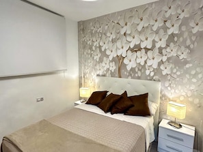 A bedroom with a bed, two bedside tables, a wall-mounted lamp, and a decorative wall panel. - Beautifully decorated apartment in Adeje, close to beach (Adeje)