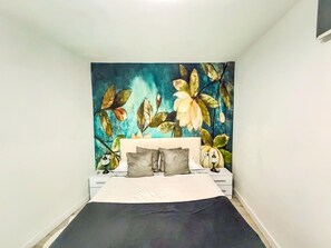 A bedroom with a bed, a nightstand, a dresser, and a wall with a floral mural. - Beautifully decorated apartment in Adeje, close to beach (Adeje)