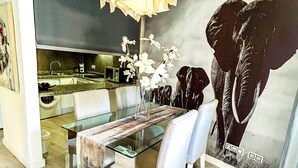 A modern dining area with a glass table, white chairs, a vase with flowers, and a large elephant mural on the wall. - Beautifully decorated apartment in Adeje, close to beach (Adeje)