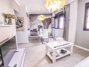 A modern living room with a white coffee table, a TV, and a dining area with chairs and a table. - Beautifully decorated apartment in Adeje, close to beach (Adeje)