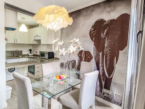 A modern kitchen with white cabinets, a granite countertop, and a dining area with a glass table and chairs. - Beautifully decorated apartment in Adeje, close to beach (Adeje)