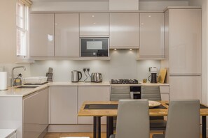 Een moderne keuken met witte kasten, een magnetron, een fornuis en een eethoek met een houten tafel en stoelen.
