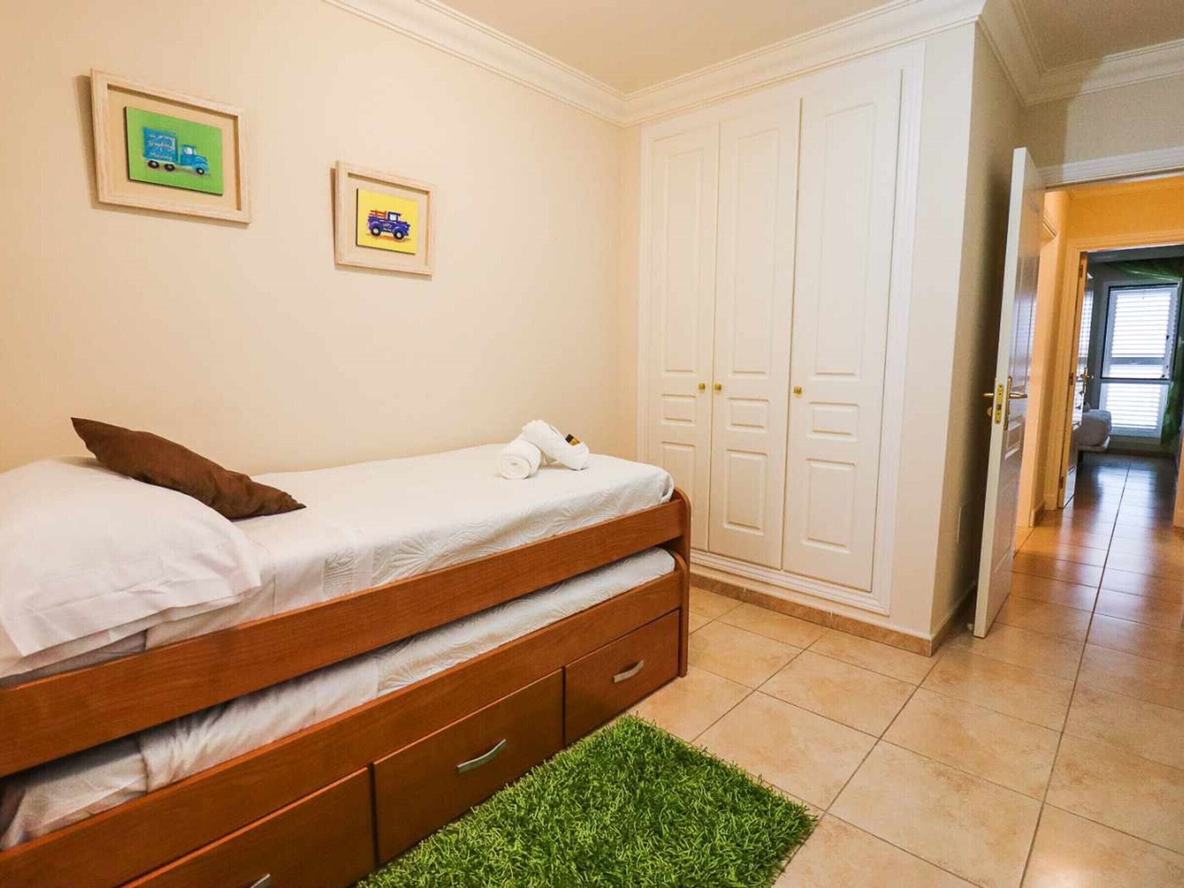 A bedroom with a bed, a green rug, and two framed pictures on the wall.