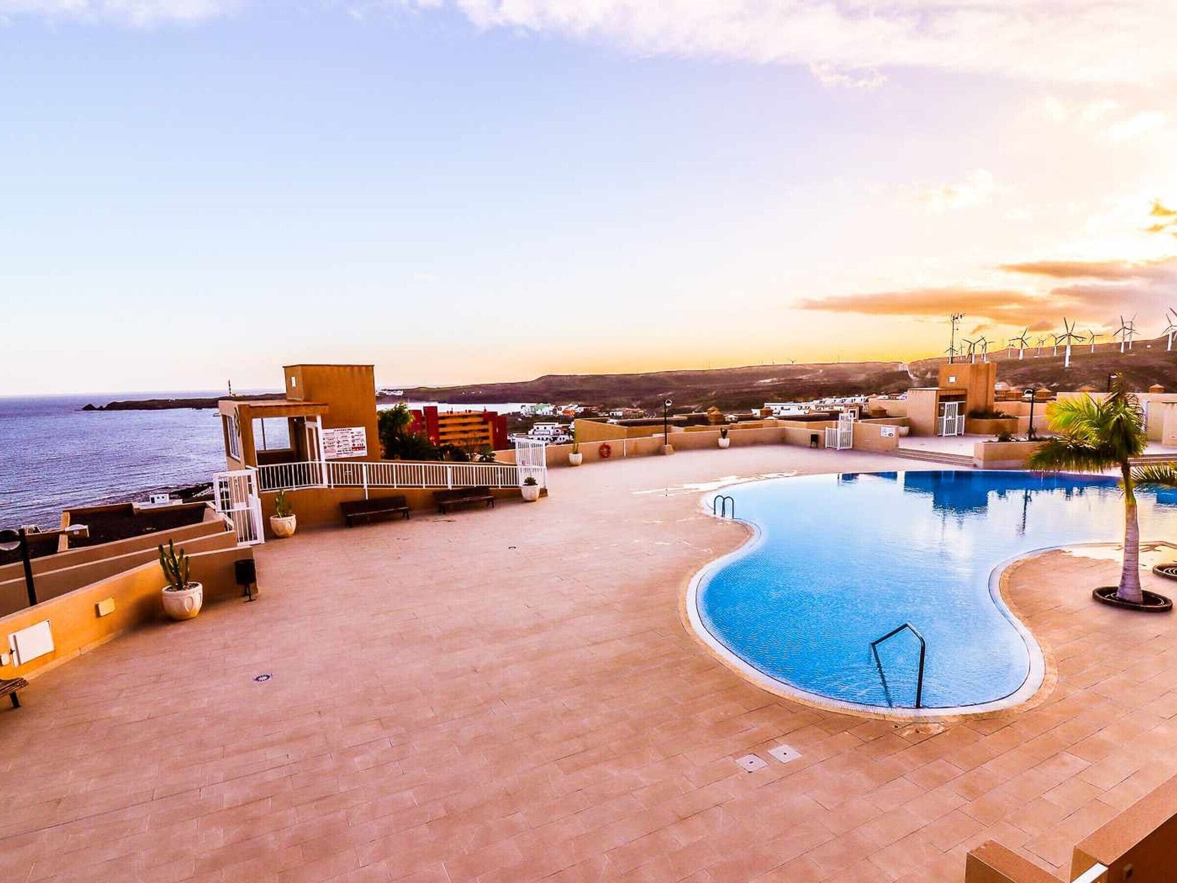 A rooftop pool with a view of the sea and wind turbines in the background.