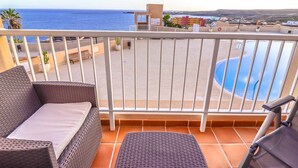 Un balcón con mobiliario de mimbre, piscina y vista al mar.