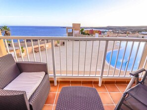A balcony with wicker furniture, a pool, and a view of the sea. - Poris de Abona Apartment with sea view, pool and parking (Porís de Abona)