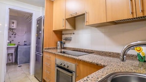 Una cocina compacta con armarios de madera, un lavamanos de acero inoxidable, un horno empotrado y un refrigerador.