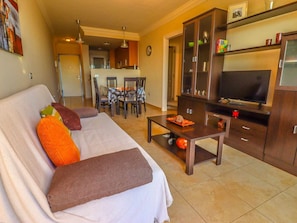 A living room with a sofa, coffee table, TV, and a dining area with chairs and a table. - Poris de Abona Apartment with sea view, pool and parking (Porís de Abona)