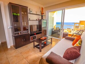 A living room with a sofa, coffee table, TV, and cabinets. There is a balcony with a view of the sea. - Poris de Abona Apartment with sea view, pool and parking (Porís de Abona)