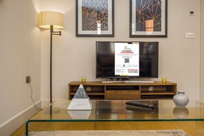 Una sala de estar moderna con una mesa de centro de vidrio, un control remoto, un jarrón y un televisor sobre un mueble de madera.
