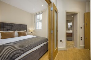 Un dormitorio con cama, mesita de noche, lámpara, ventana y puerta que da a un baño.