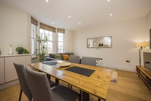 Una sala moderna con una mesa de comedor de madera, sofás grises y un ventanal con cortinas.