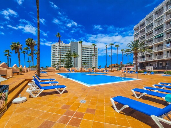 A hotel pool area with sun loungers, palm trees, and a clear blue sky. - Bright apartment with sea view - 2 guests (Costa Adeje)
