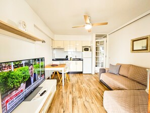 A modern living room with a television, a sofa, a dining table, and a kitchen area. - Bright apartment with sea view - 2 guests (Costa Adeje)