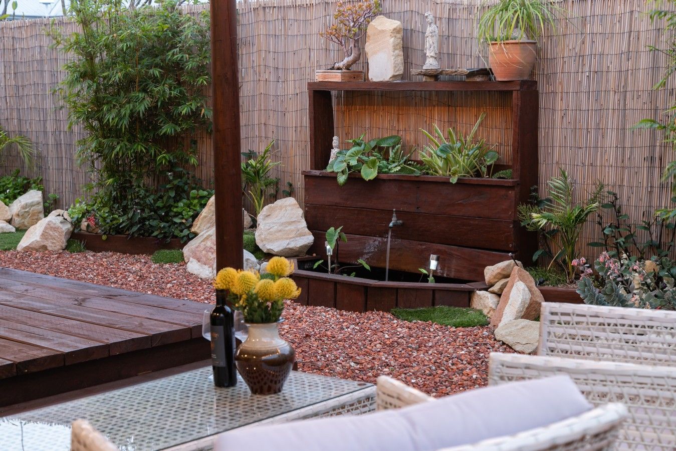 Un jardín con terraza de madera, zona de estar y valla de bambú.