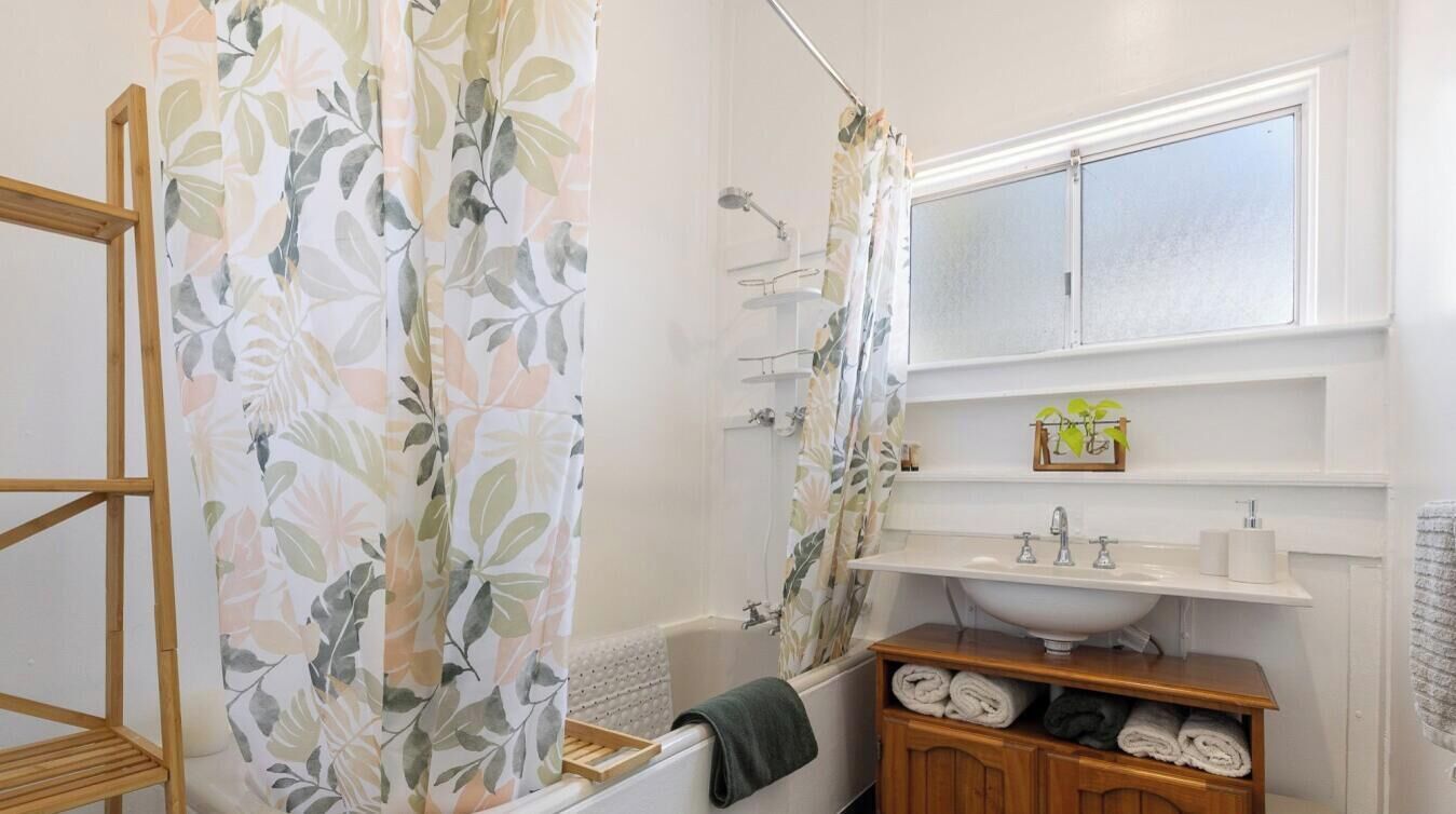 Een badkamer met een bad, een douche, een wastafel met spiegel en een plank met handdoeken.