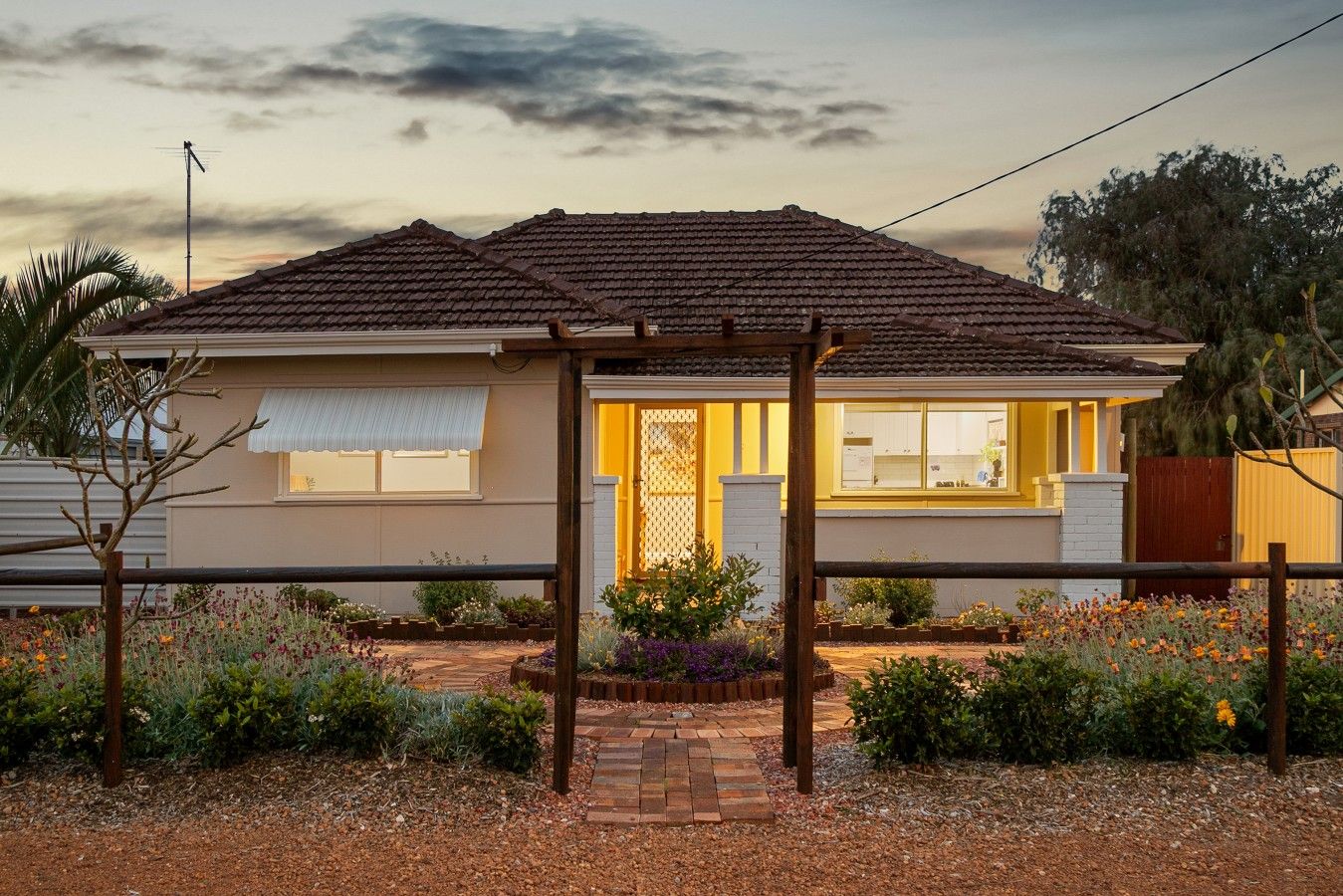 A residential house with a tiled roof, a covered porch, and a garden with various plants and flowers.