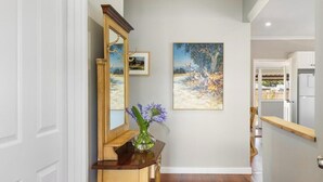 A hallway with a wooden console table, a mirror, a vase with flowers, and a painting on the wall. - The Art Lovers Cottage in Mandurah 1BR (Dudley Park)