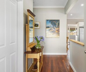 A hallway with a wooden console table, a mirror, a vase with flowers, and a painting on the wall. - The Art Lovers Cottage in Mandurah 1BR (Dudley Park)