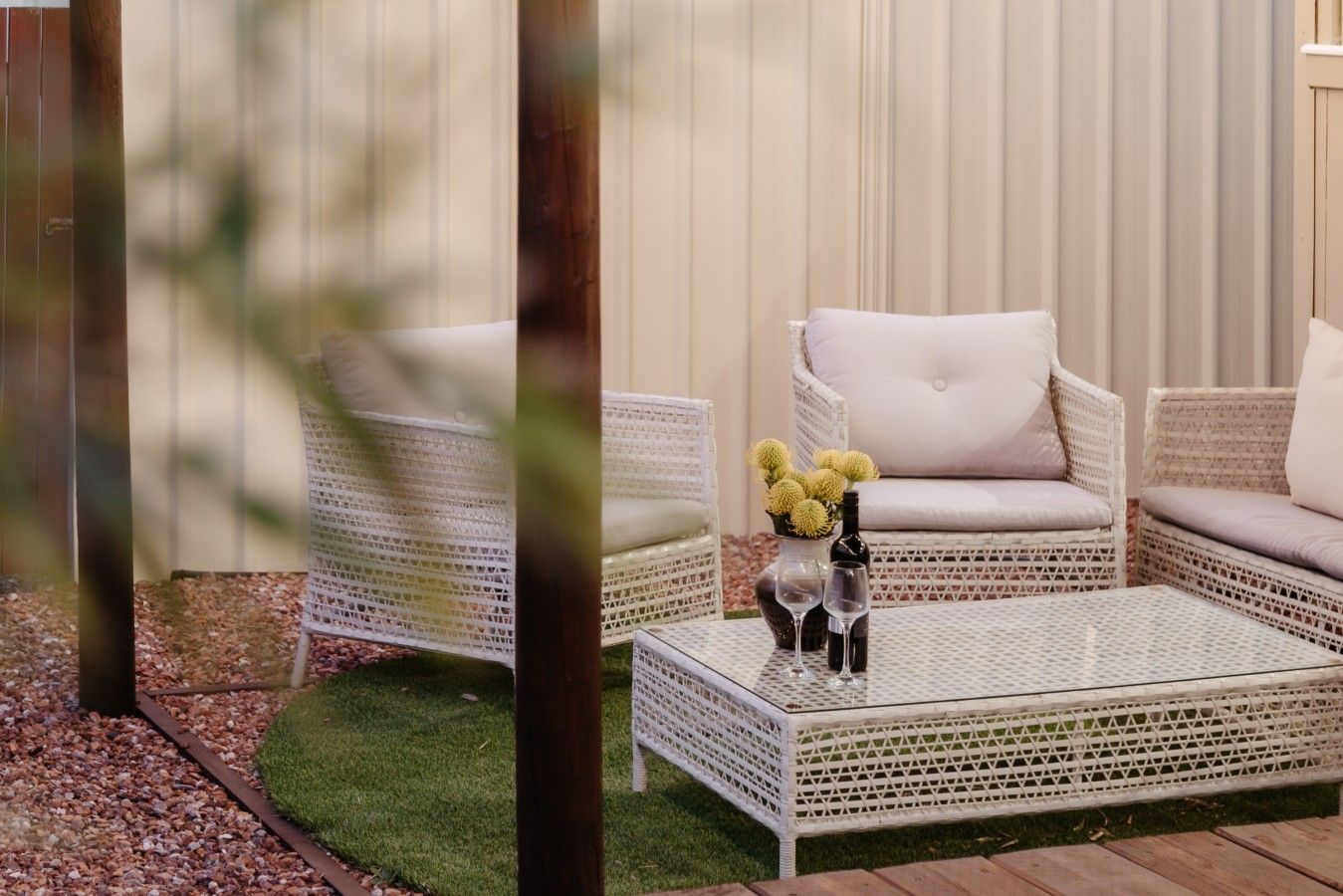 A patio area with wicker furniture, a glass table, and a vase with flowers.