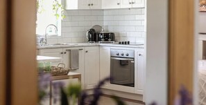 A kitchen with white cabinets, a toaster, a kettle, and an oven. - The Art Lovers Cottage in Mandurah 1BR (Dudley Park)
