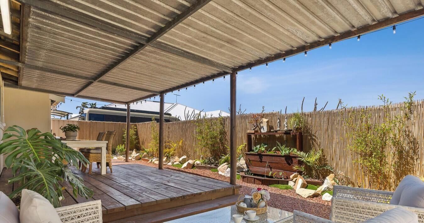 Un patio exterior techado con cubierta de madera, zona de estar y cerramiento de bambú.