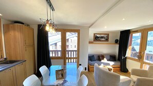 Eine moderne Küche mit Holzschränken, einem Esstisch mit weißen Stühlen, einer Couch und einer Pendelleuchte.