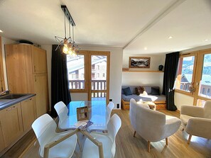 Eine moderne Küche mit Holzschränken, einem Esstisch mit weißen Stühlen, einer Couch und einer Pendelleuchte.