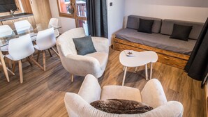 Ein modernes Wohnzimmer mit einer Couch, Sesseln, einem Couchtisch und einem Essbereich mit Stühlen und einem Glastisch.