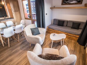 Ein modernes Wohnzimmer mit einer Couch, Sesseln, einem Couchtisch und einem Essbereich mit Stühlen und einem Glastisch.