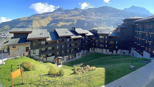 Ein Bergresort mit mehrstöckigen Gebäuden, einem grasbewachsen Innenhof und Blick auf schneebedeckte Berge.