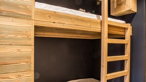 Ein Etagenbett mit Holzlade, einem kleinen Stofftier und einer dunklen Wand.