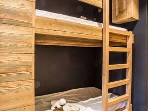 Ein Etagenbett mit Holzlade, einem kleinen Stofftier und einer dunklen Wand.