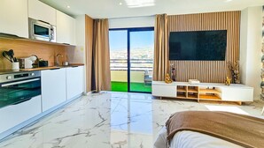 A modern hotel room with a kitchen, a large TV, and a balcony with a view. - Luxury studio, sea view in Tenerife (Playa Paraiso)
